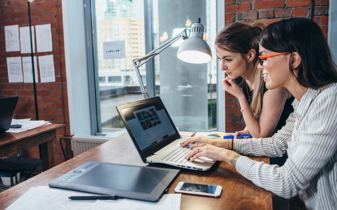 Two women working on new website design choosing pictures using the laptop surfing the internet.